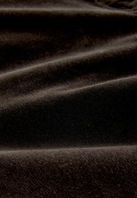 Čierny zamatový materiál s jemnou, nadýchanou textúrou, obsahujúci jemné záhyby a hladký povrch, ktorý odráža svetlo z rôznych uhlov.