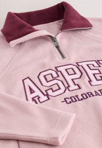 Ljusrosa fleecepullover med vinröd krage och dragkedja, med stor "ASPE" och mindre "COLORADO" text på framsidan.