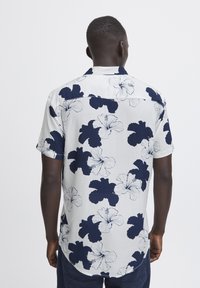 Camicia a maniche corte con sfondo bianco e grandi motivi di fiori di ibisco blu scuro. Tessuto leggero con una vestibilità comoda.