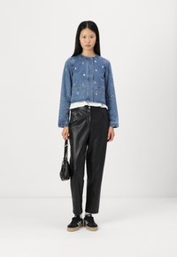 Denim jakna z okrasnimi očesi, skrajšana zasnova, nosi se preko bele majice in črnih hlač iz umetnega usnja, v kombinaciji s črnimi športnimi copati.