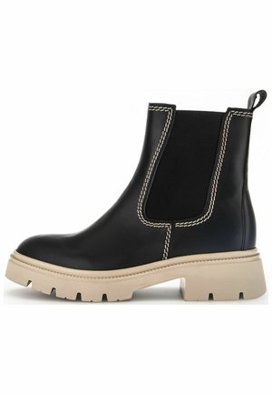 Black leather ankle boot with elastic side panels, beige chunky sole, and contrasting white stitching along the seams and edges.
