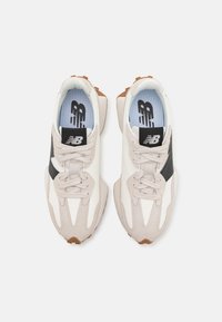Zapatillas con parte superior de malla beige y blanca, acentos negros, suela de goma y plantillas azul claro. Cuentan con cierre de cordones y un diseño curvado.