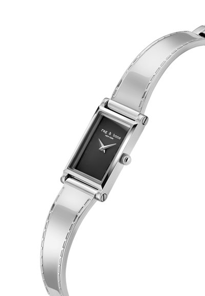 Hõbedane ristkülikukujuline käekell musta näo, minimaalsed tundemarkerid ja poleeritud metalline rihm, kus on peened õmblusdetailid.