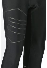 Schwarze Sportleggings mit einem glänzenden schwarzen Streifenmuster an der äußeren Oberschenkelpartie und Flachnähten für verbesserte Langlebigkeit.