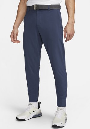 Pantaloni tapered blu navy realizzati in tessuto leggero, con una texture liscia, passanti per cintura e vestibilità slim, abbinati a sneaker bianche.