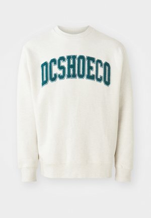 Light beige sweatshirt made of soft fabric, featuring a teal embroidered "DCSHOECO" text across the chest. Ribbed cuffs and hem.
