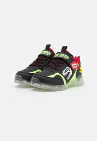 S ténis pretos com detalhes em verde néon, parte superior texturizada, colarinho acolchoado e sola clara. Apresenta gráficos de dinossauros e a marca Skechers.