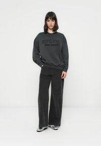 Felpa grigia scura con logo in rilievo "Ripcurl Surf Sports", abbinata a pantaloni larghi scuri e scarpe argentate lucide.
