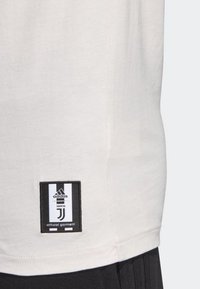 Crèmekleurig stoffen t-shirt met een zwart-witte label met het Adidas-logo en de tekst "Juventus", gestikt aan de onderzijde.