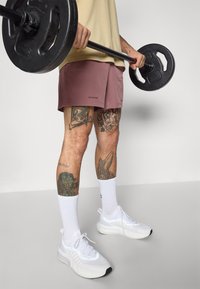 Gewichtheber-Shorts aus Blush-Stoff mit strukturierter Oberfläche, kombiniert mit weißen Sportschuhen und knielangen weißen Socken.