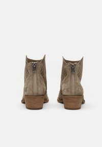 Bottines en daim taupe perforé avec un petit talon en bois et des fermetures éclair à l'arrière. Présentent un logo papillon sur le côté extérieur.