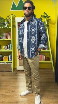 Chemise : bleu marine avec motifs géométriques blancs, à boutons, manches longues. Pantalon : beige clair, coupe droite. Chaussures : baskets blanches.