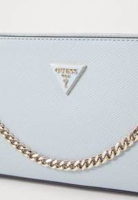 Sac synthétique texturé bleu clair avec un logo en argent triangulaire et une finition chaînon en ton or le long du bord.
