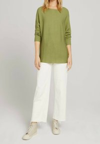 Olivgrüner gerippter Pullover mit lockerer Passform, kombiniert mit weiten weißen Hosen und hellbeigen High-Top-Sneakern mit Schnürdetails.