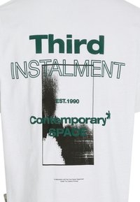 White cotton t-shirt featuring green and black printed text reading "Third INSTALMENT EST. 1990 Contemporary SPACE" and graphic details.