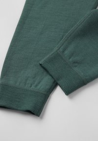 Teal langemouwig kledingstuk met close-up van ribbelmanchetten en gedetailleerde stitching op zachte, gebreide stof.
