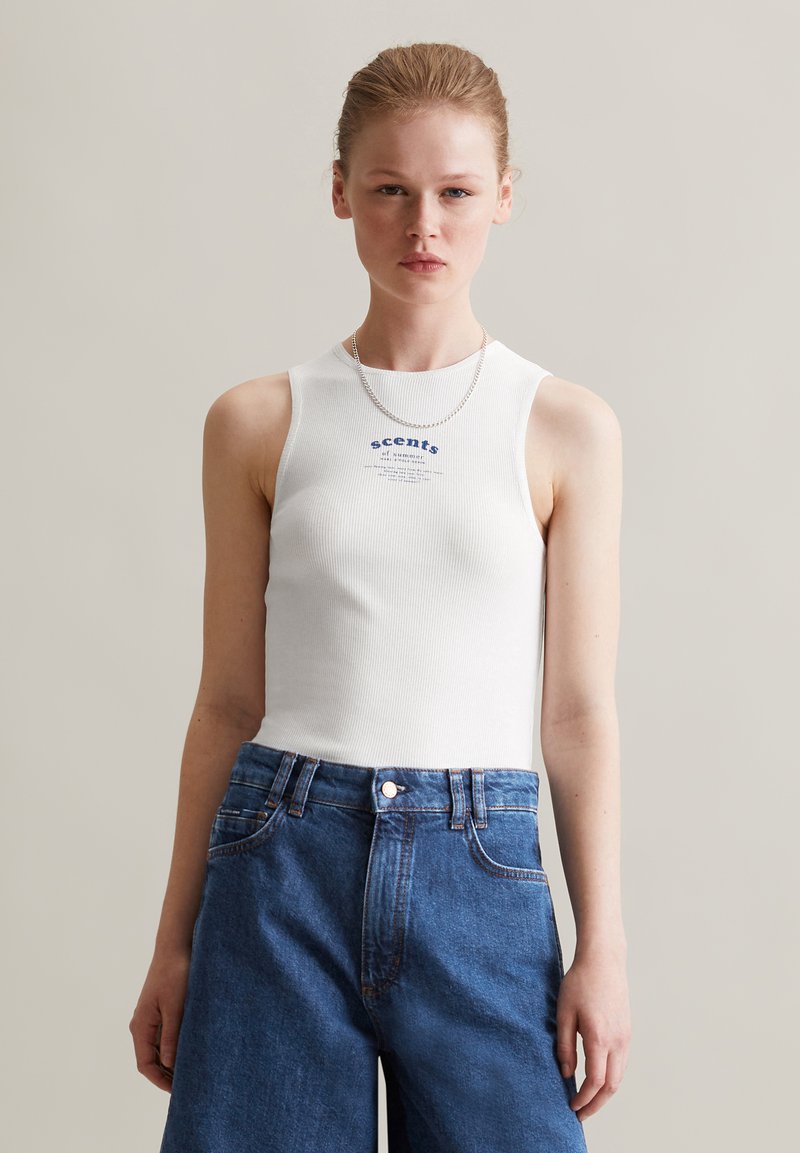 Witte geribde tanktop met een ronde halslijn, met blauwe tekst en een grafische print. Gecombineerd met hoge, blauwe denim shorts.