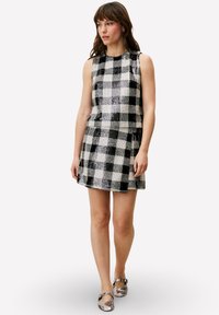 Robe à manches courtes, longueur au genou, présentant un motif à carreaux noir et blanc avec une finition texturée. Associée à des chaussures plates métalliques.