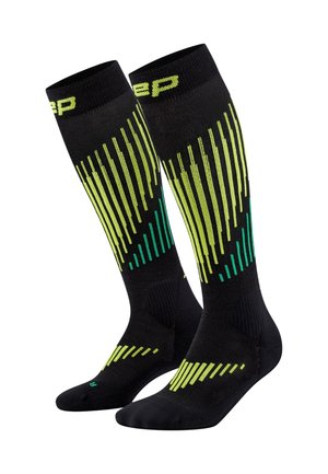 Calzini sportivi neri al ginocchio con motivi a strisce verticali in neon giallo e verde e testo del marchio vicino al bordo superiore.