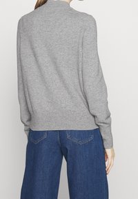 Pull en maille grise avec un col haut, des poignets et un ourlet côtelés, associé à un jean denim bleu à jambes larges. Vue de dos mettant en valeur la texture.