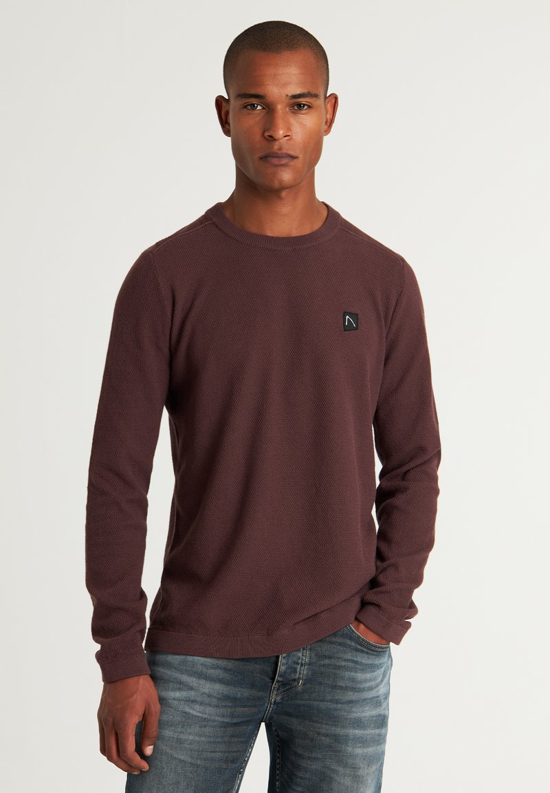Sweatshirt bordo cu mâneci lungi din material texturat, decolteu rotund, manșete ribbate și o mică etichetă logo neagră pe piept.