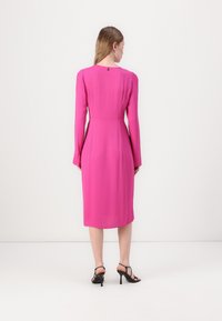 Fuksia midi-mekko, jossa on pitkät hihat, istuva vyötärö ja hienovarainen takatieto. Yhdistetty mustiin remmisandaaleihin, joissa on korko.