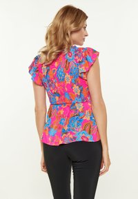 Blomstret peplum-top i pink, med blå og orange blomsterprint, flæseærmer og struktureret stof. Matchende med sorte bukser.