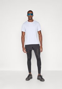 Világoskék, rövid ujjú Nike póló, fekete nadrág fekete kompressziós leggings felett. Sportcipők texturált fekete anyagból, kék napszemüveg.