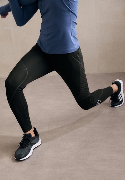 Schwarze Sportleggins mit strukturiertem Design, kombiniert mit einem blauen Langarmshirt und schwarzen Laufschuhen. Glattes, eng anliegendes Material.
