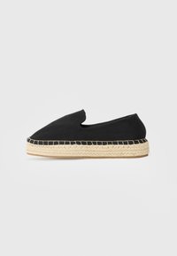 Espadrille noire en toile à enfiler avec semelle en jute tressée naturelle et couture visible autour du bord, vue de côté sur fond blanc.
