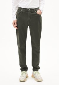 Olijfgroene katoenen broeken met een klassieke pasvorm, vijf zakken en een knoopsluiting. Geroepen met lichtgekleurde sneakers.