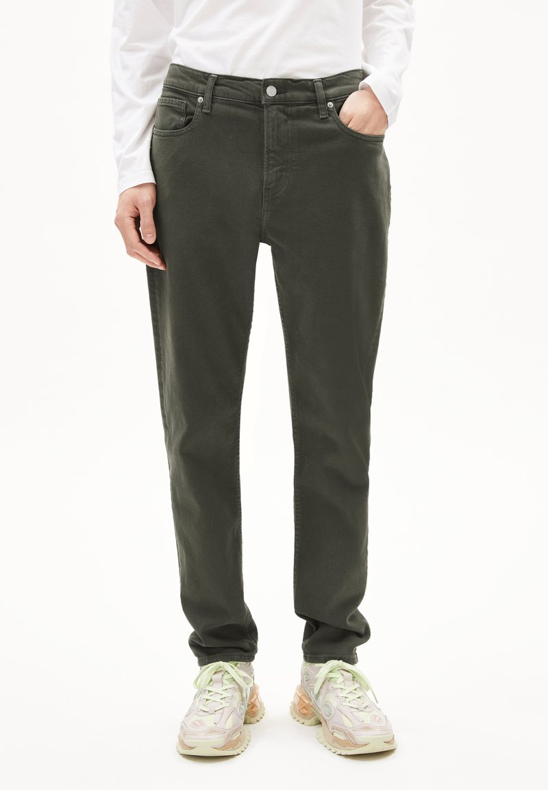 Olijfgroene katoenen broeken met een klassieke pasvorm, vijf zakken en een knoopsluiting. Geroepen met lichtgekleurde sneakers.