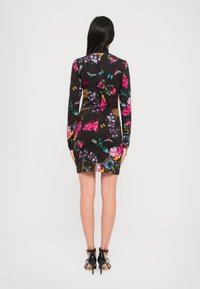 Zwart aansluitend jurkje met lange mouwen, levendige bloemen- en vlinderprint, gladde stof, boven de knie lengte, gecombineerd met zwarte hoge hakken.