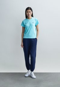 Ανοιχτό μπλε βαμβακερό t-shirt με κοντά μανίκια και μικρό λογότυπο, συνδυασμένο με μπλε ναυτικό παντελόνι jogger και λευκά αθλητικά παπούτσια. Απλό, καθημερινό ντύσιμο.