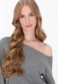 Pulover tricotat gri, cu umerii descoperiți, cu o textură moale. Părul lung, ondulat, blond și cerceii din perlă completează o expresie neutră.