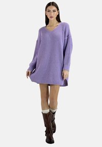 Paarse gebreide sweaterjurk met een V-hals, oversized mouwen en een gestructureerde stof, gecombineerd met bruine laarzen en crèmekleurige sokken.