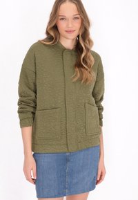 Quiltad olivgrön jacka med blommönster, med rund halsringning, tv�å framfickor och ribbade ärmslut, tillsammans med en denimkjol.