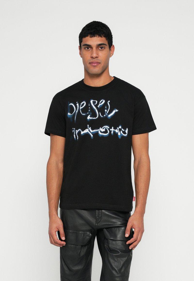 Μαύρο βαμβακερό μπλουζάκι με παραμορφωμένο λευκό και μπλε λογότυπο. Στρογγυλή λαιμόκοψη, κοντά μανίκια και κανονική εφαρμογή. Λεπτομέρεια υφής στο ύφασμα.