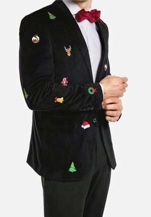 Muž v černém saku se vyšitými vánočními ikonami, včetně stromku, věnce, Santa Clause, pudinku, soba, zvonku a červeného motýlka.