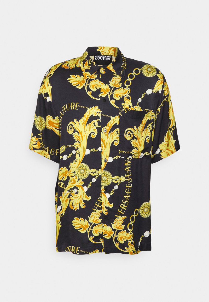 Chemise à manches courtes en soie noire avec de grands motifs baroques jaunes et des accents de texte. Comprend une poche avant et une fermeture à boutons.