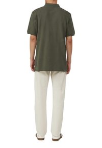 Dunkelgrünes kurzärmliges Poloshirt mit klassischem Kragen, von hinten gezeigt, kombiniert mit hellbeigen Hosen und braunen Sandalen.