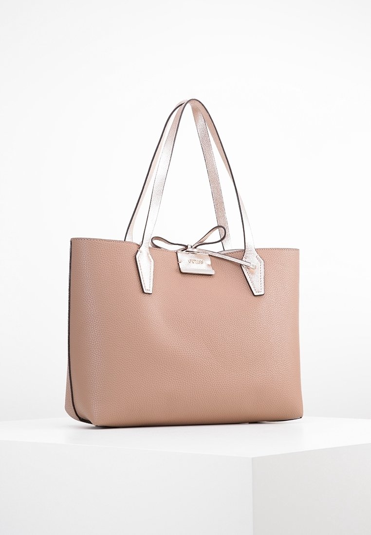 Sac fourre-tout en cuir beige à texture lisse, avec des accents métalliques argentés, deux poignées robustes et une petite plaque nominative fixée à l'avant.