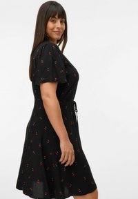 Robe noire avec de courtes manches bouffantes, arborant un motif de cerises. La taille à cordon crée une silhouette fluide. Texture de tissu douce.