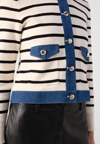Cardigan a righe realizzato in tessuto a maglia nei colori crema e nero, con dettagli in denim, due tasche sul petto e bottoni argentati sulla parte frontale.