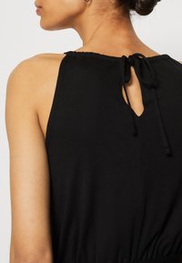 Top noir sans manches avec une découpe en forme de trou de serrure à l'arrière, doté d'une fermeture à nouer et d'un col froncé. Texture lisse et coupe décontractée.