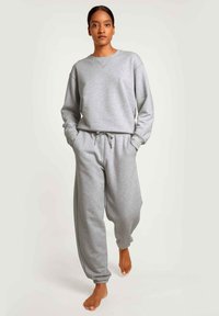 Felpa grigia con vestibilità rilassata e polsini a costine, abbinata a pantaloni della tuta grigi a vestibilità larga con vita elasticizzata e coulisse.