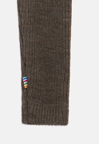 Manga de camisola castanha de malha com textura canelada, apresentando uma etiqueta às riscas multicolor perto da bainha.