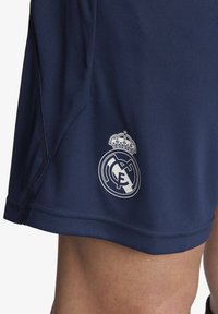 Pantalones cortos deportivos azul marino hechos de un tejido que absorbe la humedad, con un logo bordado en blanco del Real Madrid en la parte inferior izquierda.
