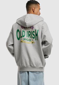 Pelēks sporta krekls ar lielu daudzkrāsainu "OLD IRISH MOB" grafiku uz muguras, ar brīvu piegriezumu un ribotām piedurknēm un apakšmali.