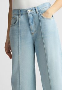 Jeans de mezclilla azul claro con corte recto, que cuentan con dos bolsillos frontales, un cierre de cremallera y costuras en color contrastante a lo largo de las costuras.